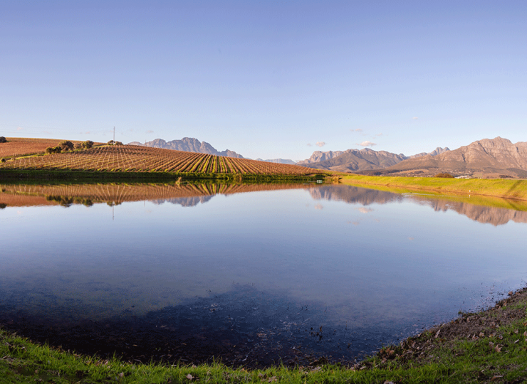 Scenic pond reflecting mountains and farmland under a clear sky
