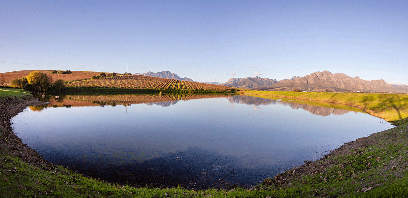 Scenic pond reflecting mountains and farmland under a clear sky