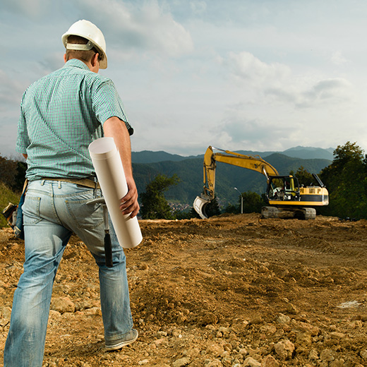 Contractor reviewing pond construction plans while excavator prepares the site